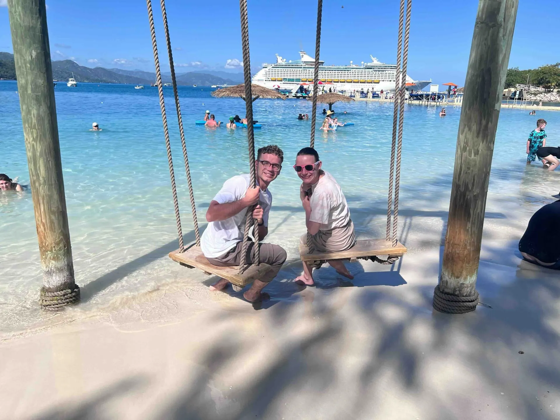 Two friends on beach swings with the ship in the distance
