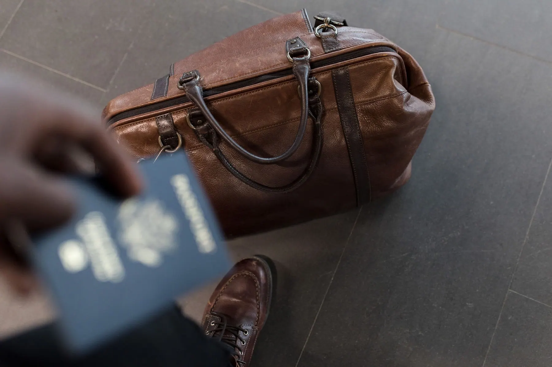 A passport held out beside a leather travel bag