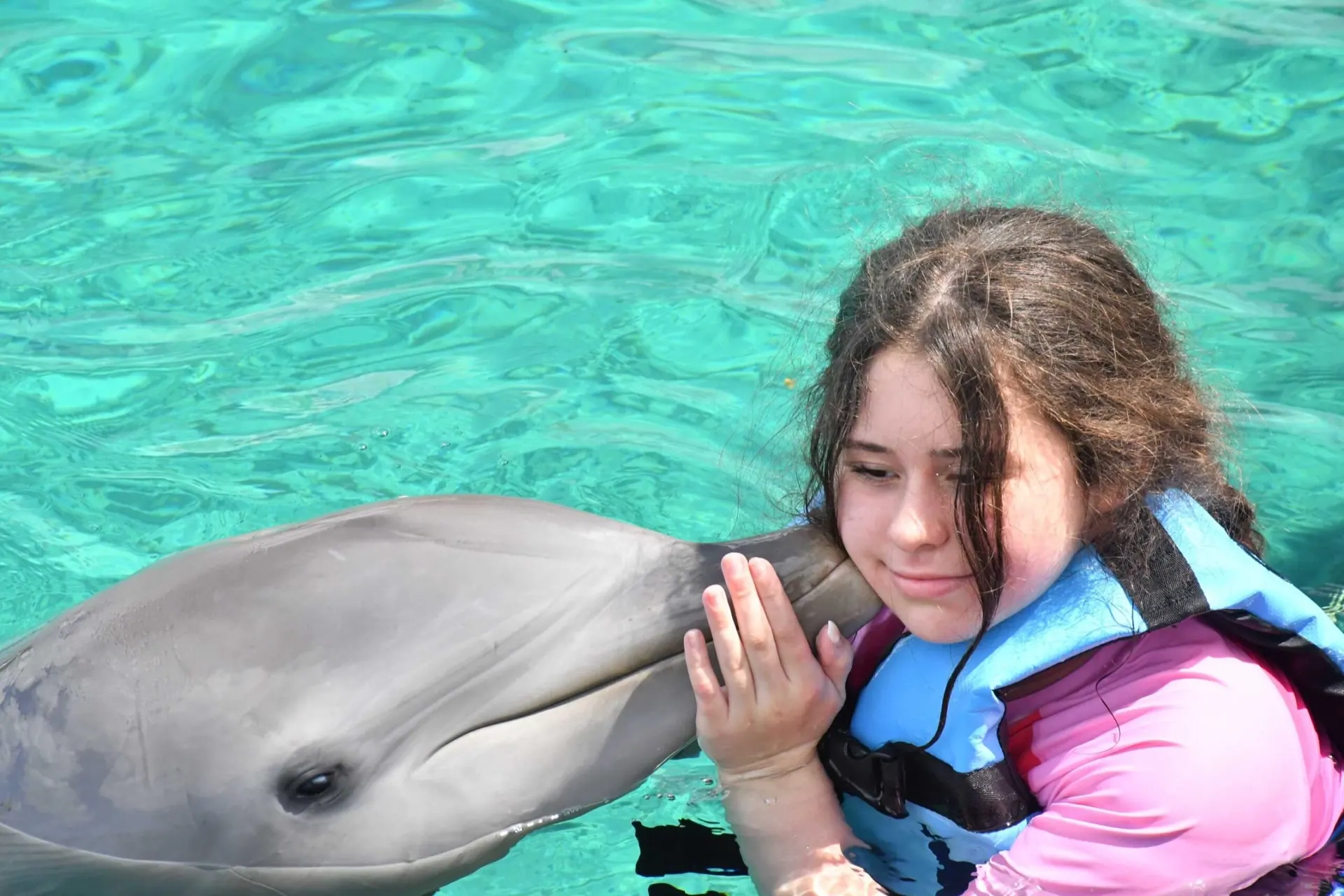 A girl getting a kiss from a dolphin in turquoise water